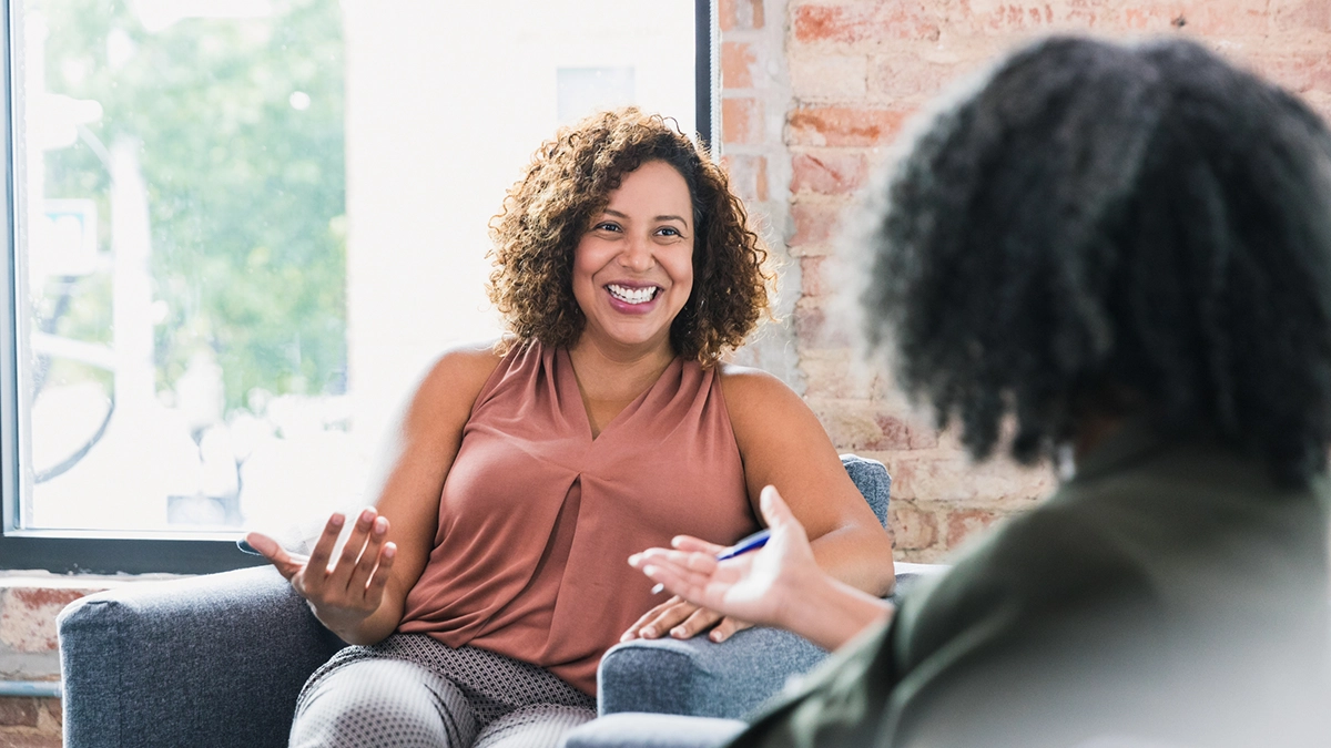 Two women talking during a mental health counseling session in a bright, sunlit therapy office in Orange County, California.